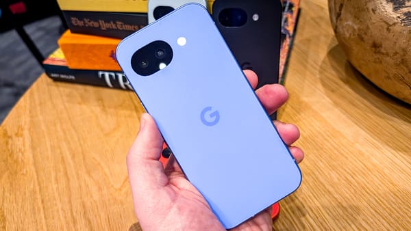 A photo of a person holding the Pixel 10a with a backdrop of a meeting room 